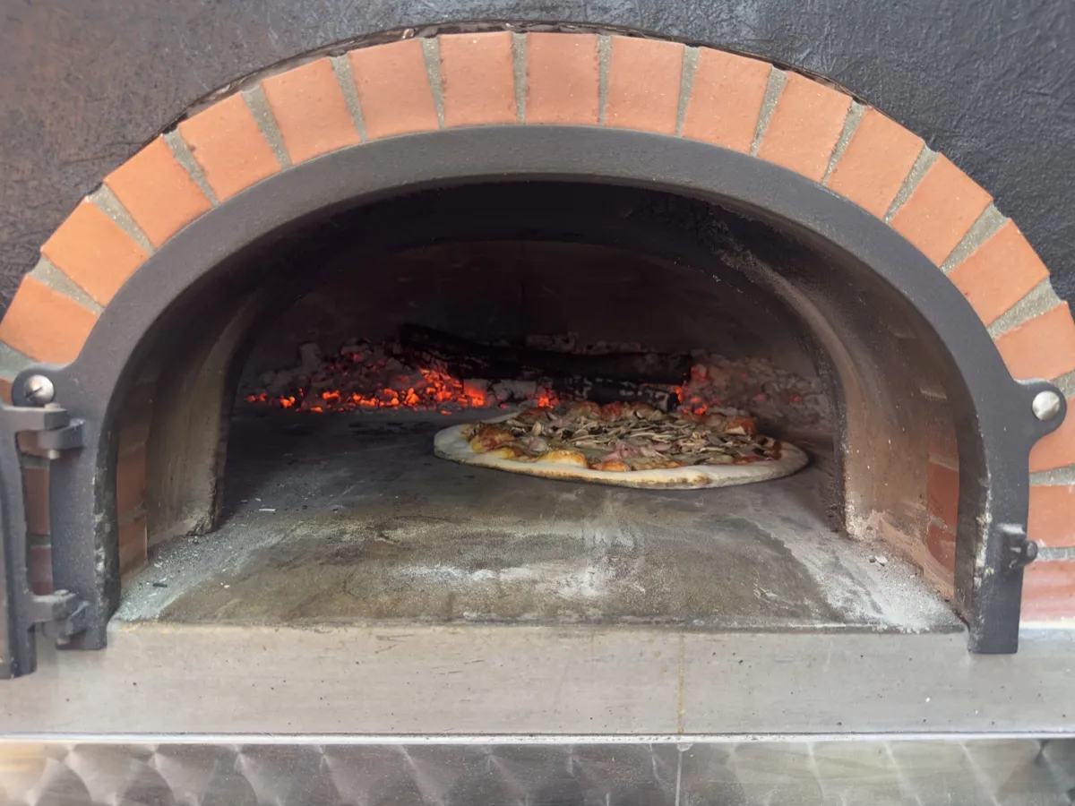 Une pizza glisse sur la pelle dans le four à bois, Pizza Thaololo Pierrevert