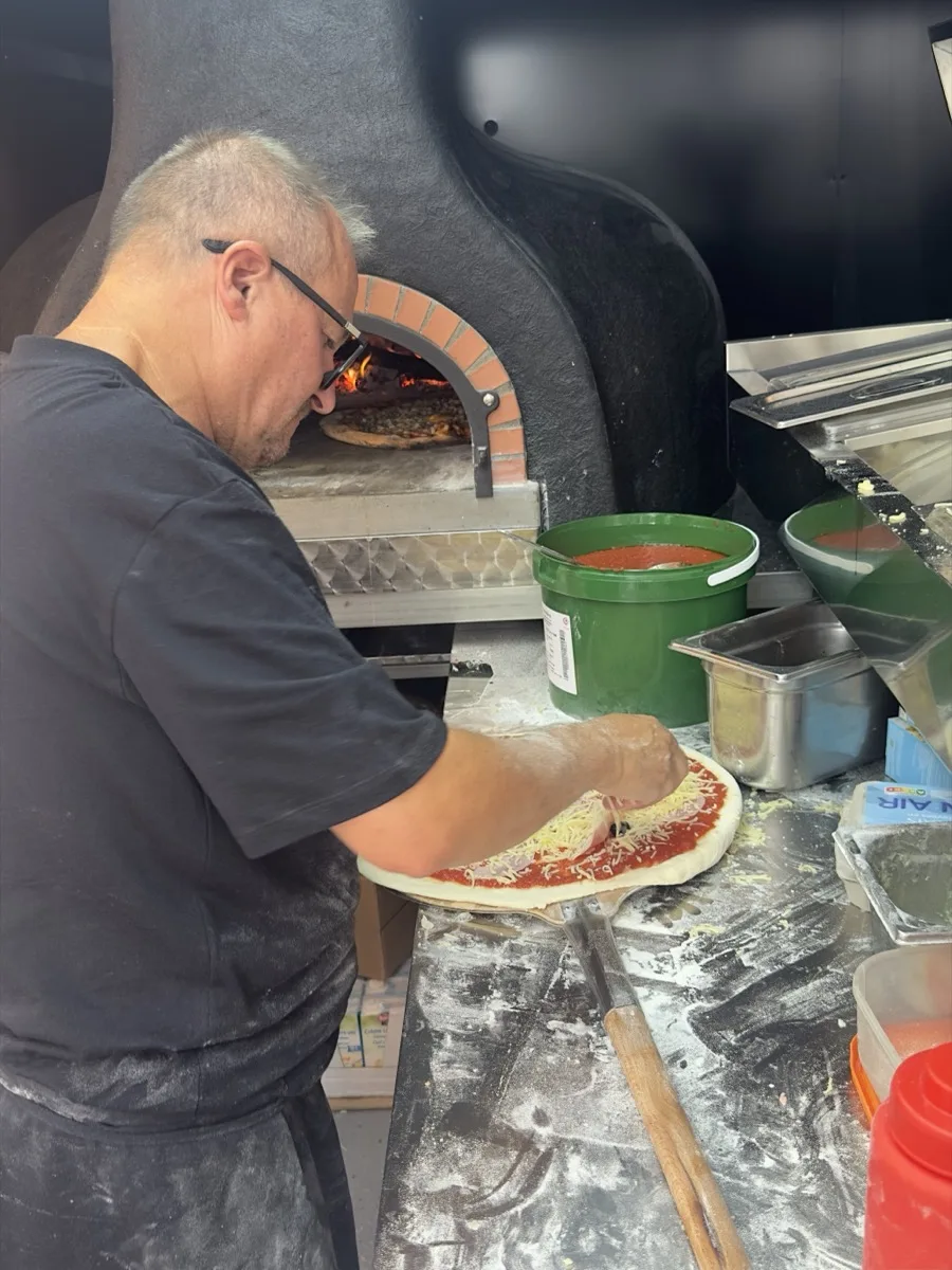 Thao garnit une pizza devant le four à bois allumé, food truck Pizza Thaololo à Pierrevert